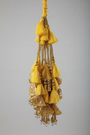A decorative hanging ornament with multiple yellow tassels, gold beaded strands, and embellished gold and silver fabric tiers, photographed indoors against a light wall.