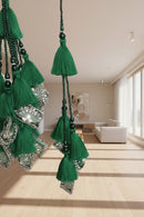 Green tassel ornaments hanging in a store or workshop setting, with a blurred background showing stacked items and a table.